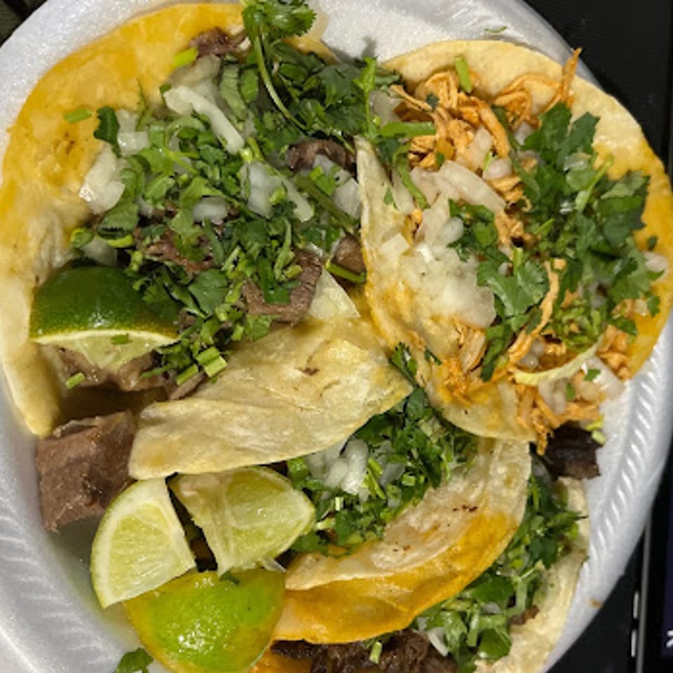 A close-up of three Mexican street tacos with meat, cilantro, onions, and lime wedges.