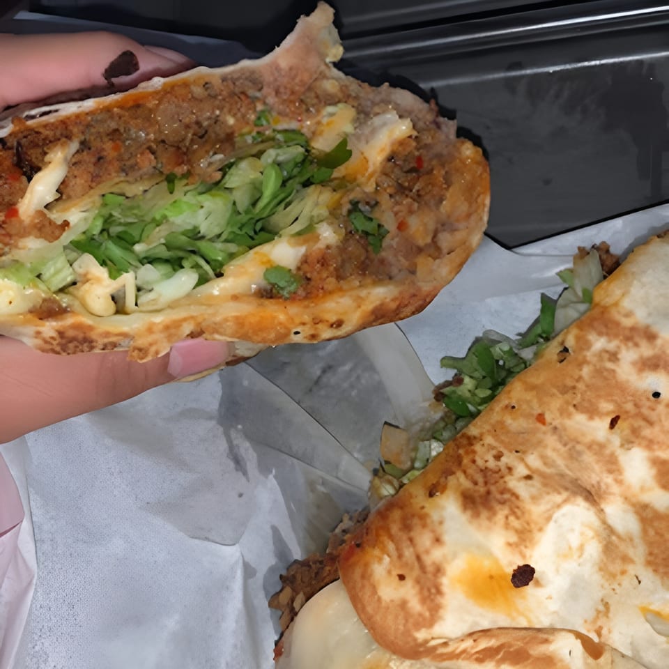 A hand holds a large, cut-open Mexican burrito filled with meat, cheese, and lettuce.