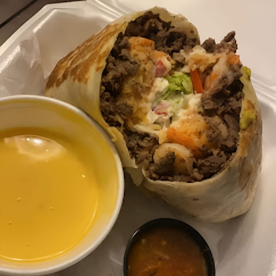 A large, cut open burrito filled with meat, rice, and vegetables, served with cheese dip and salsa.
