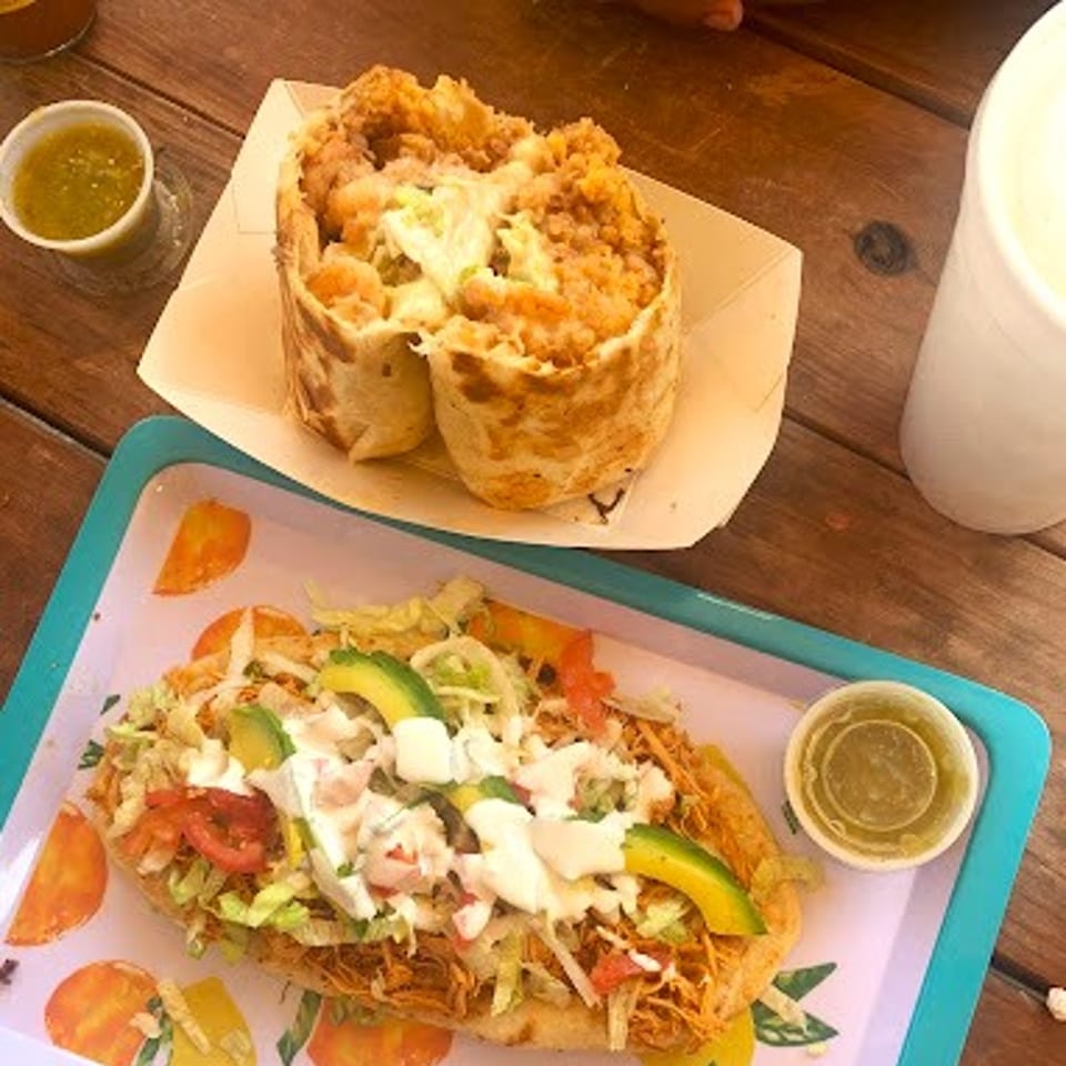 A burrito and a large taco, both topped with fresh ingredients, on a wooden table.