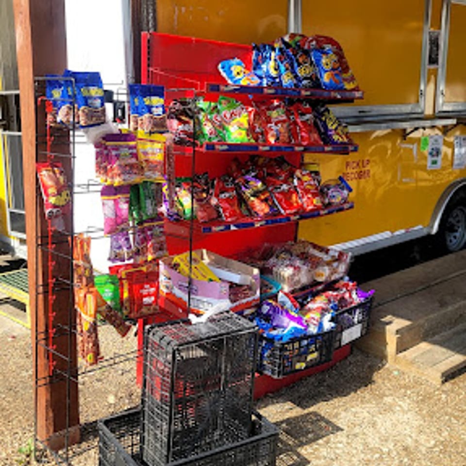 A red snack display rack filled with various bags of chips and candies, next to a yellow food truck.